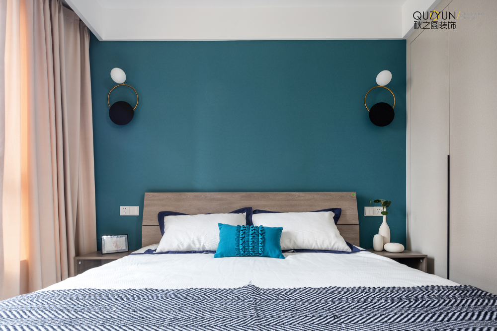 以孔雀蓝背景墙辅助金属吊灯的优雅搭配,床头摆放的禅意花卉让简约的